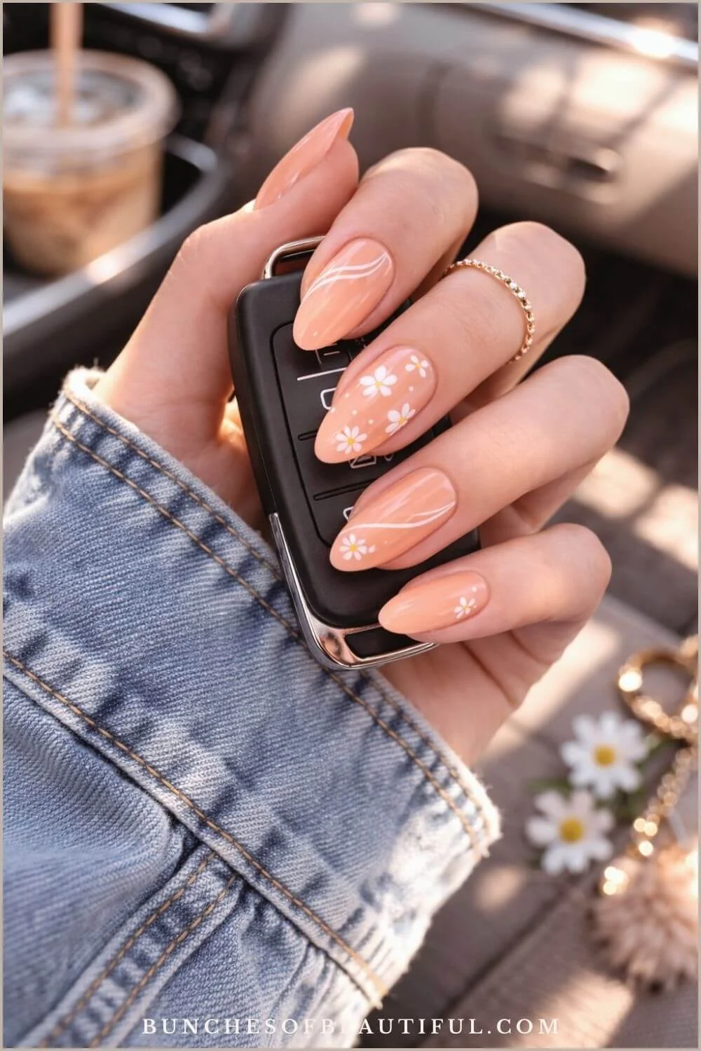 Peach spring nails with white daisy nail art and subtle swirl accents on almond shaped nails while holding a car key.