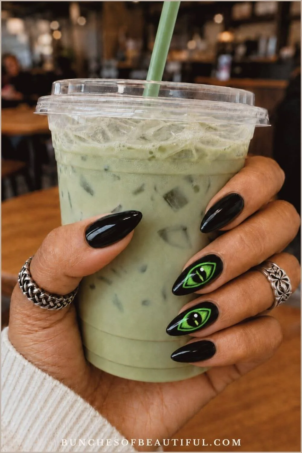 Glossy black almond nails with vivid neon green eye accents while holding an iced matcha drink.