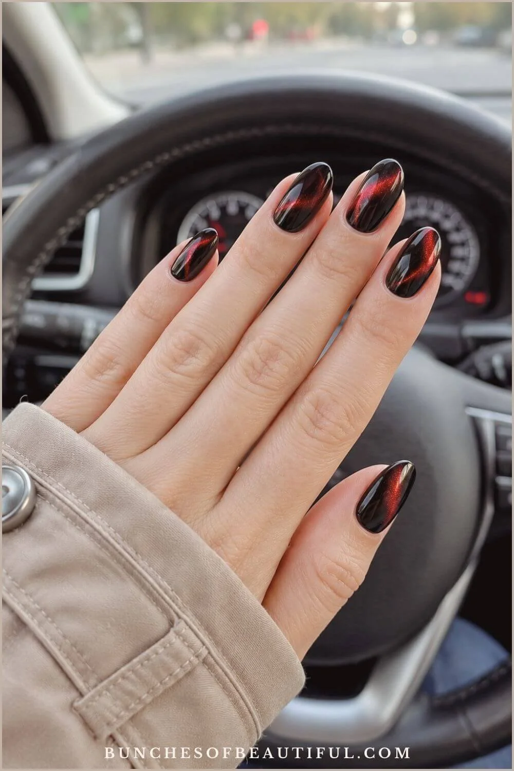 Almond-shaped black nails with glowing red cat-eye accents displayed in front of a car steering wheel.