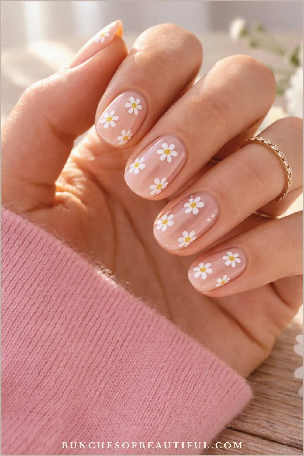 Cute spring nails with small white daisy flowers on a soft pink base with short rounded nails and glossy finish.