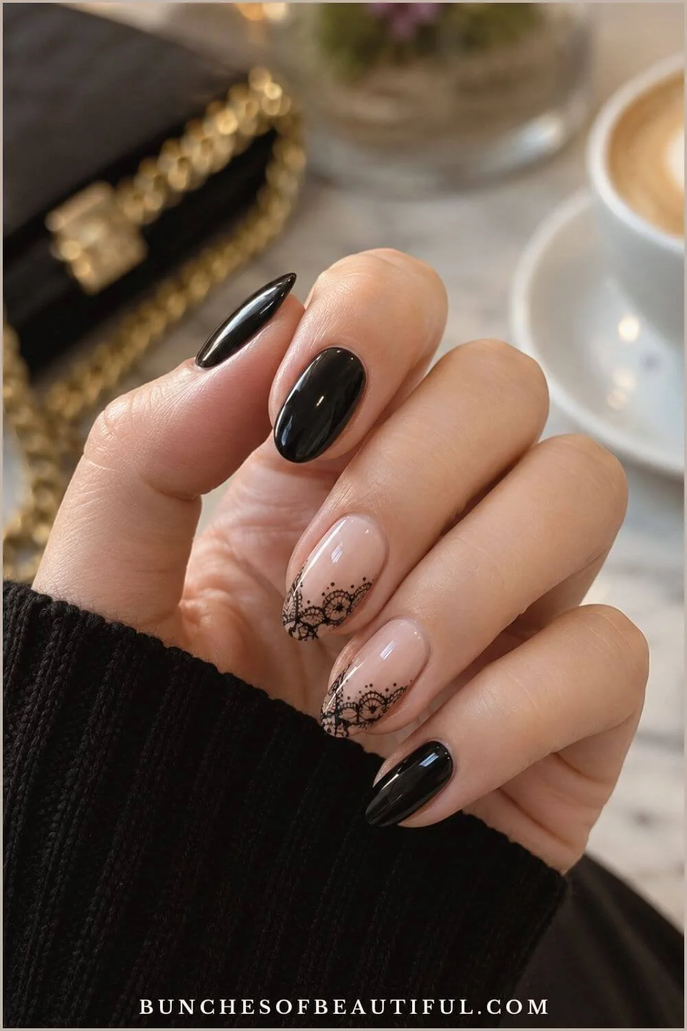 Glossy black and nude almond nails with delicate black lace accents photographed at a café table.