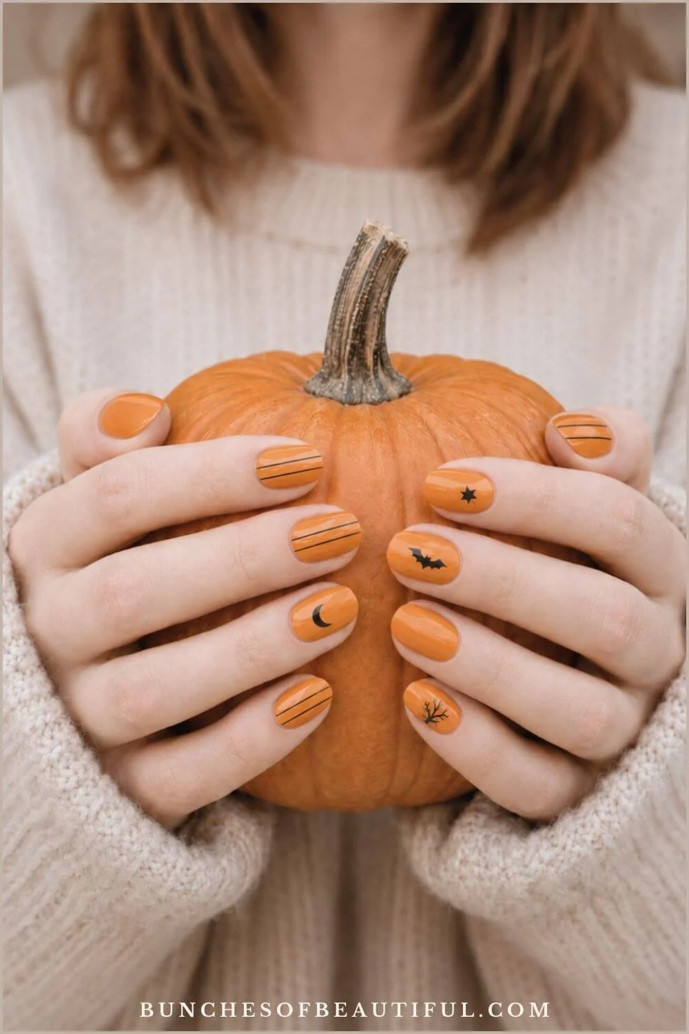 Short orange nails with black moons, bats, stars, branches, and fine stripes while holding a pumpkin.