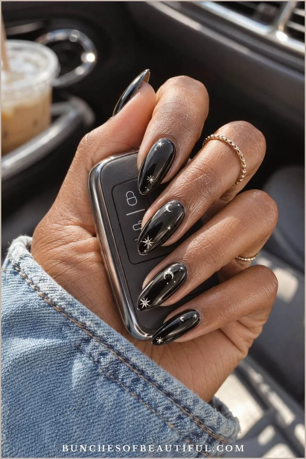 Glossy black almond nails decorated with silver moons and stars while holding a car key.