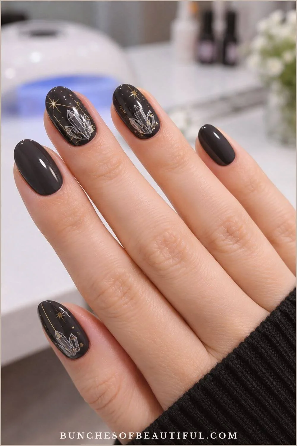 Glossy charcoal-black oval nails with white crystal illustrations and delicate gold stars in a nail salon.