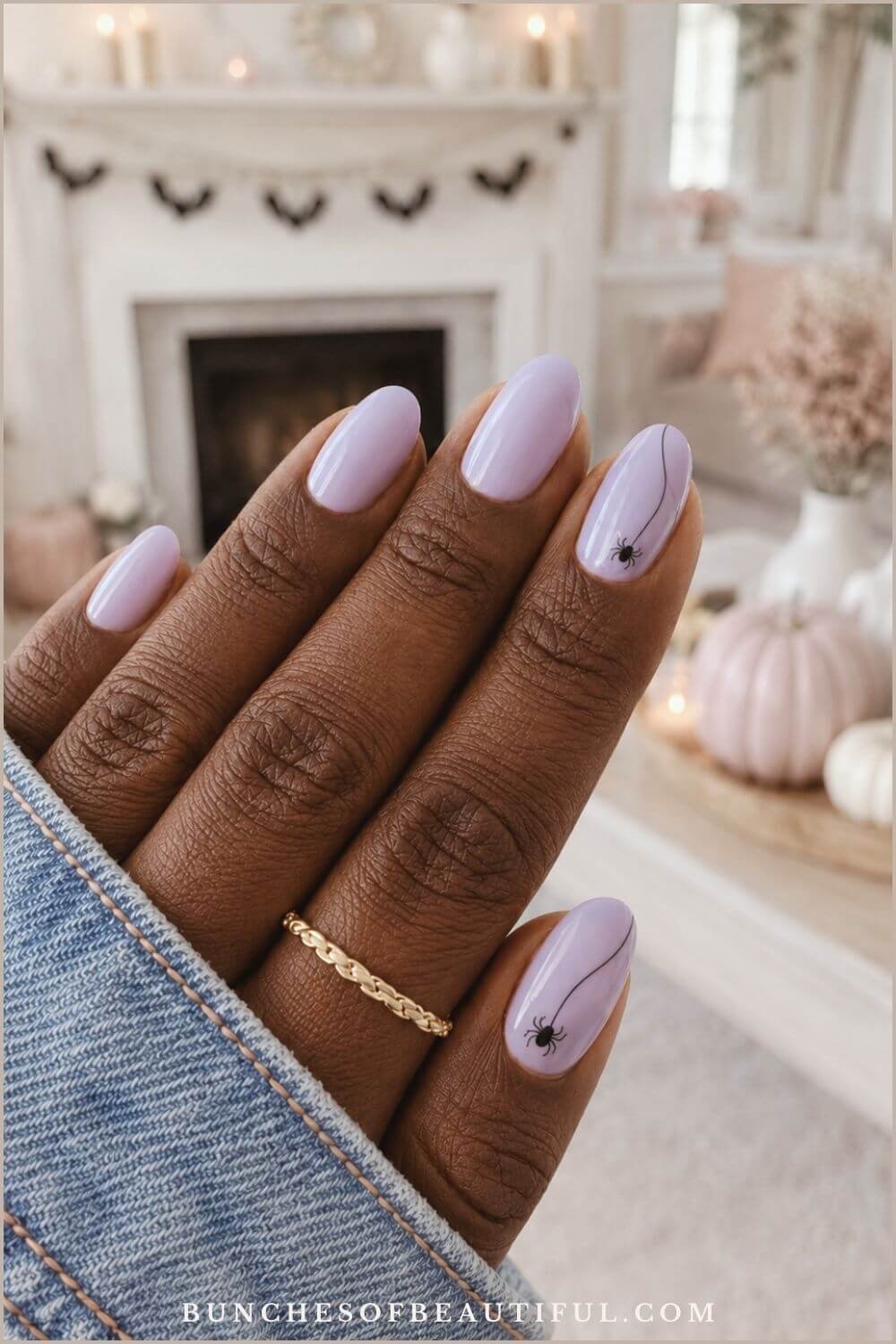 Soft lavender oval nails with two small black spiders hanging from fine curved lines in a pastel Halloween setting.
