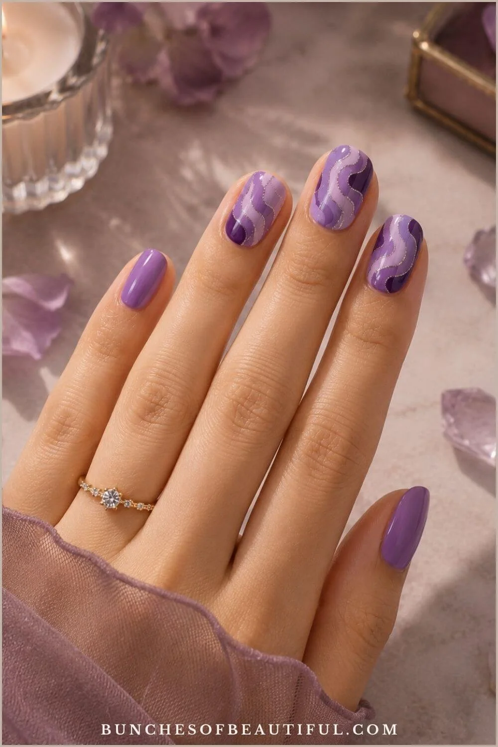 Short oval nails with layered lavender and deep-purple wavy swirls outlined in fine silver glitter beside purple crystals.