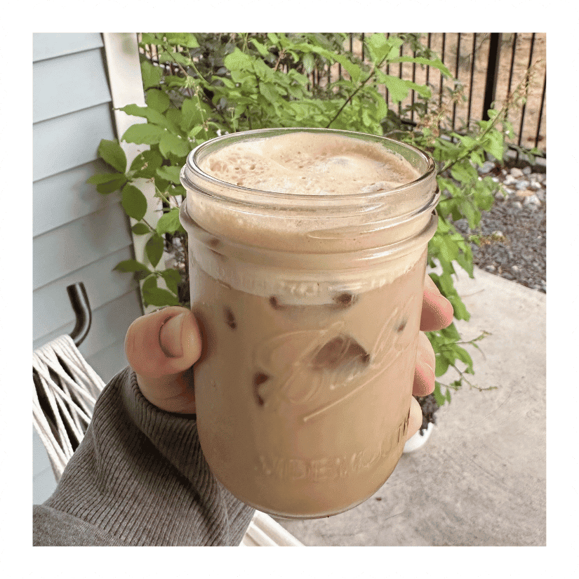 Iced coffee with cold foam in a mason jar, held on a backyard patio