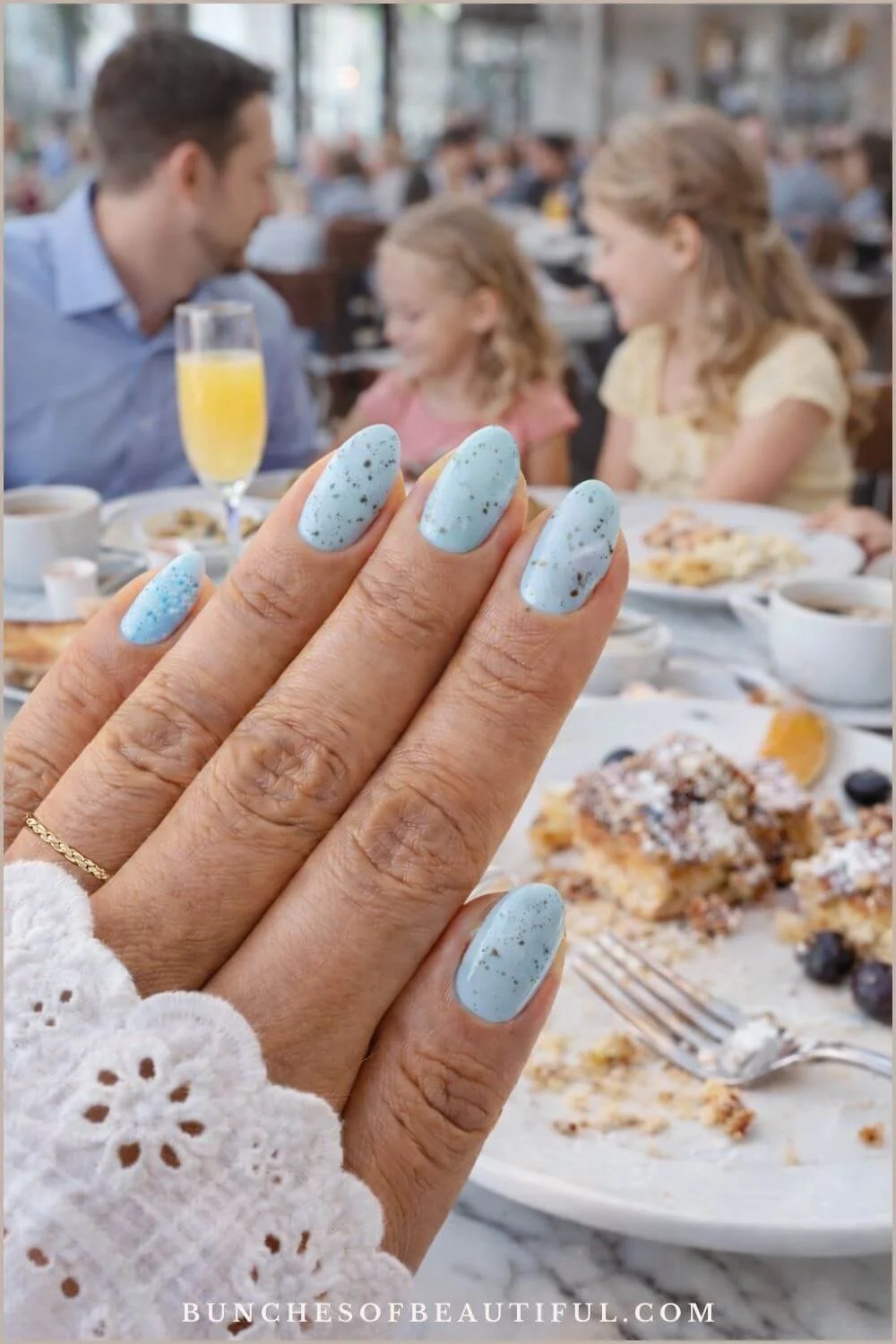 Light blue speckled Easter egg inspired spring nails on almond shaped nails at a bright family brunch table.