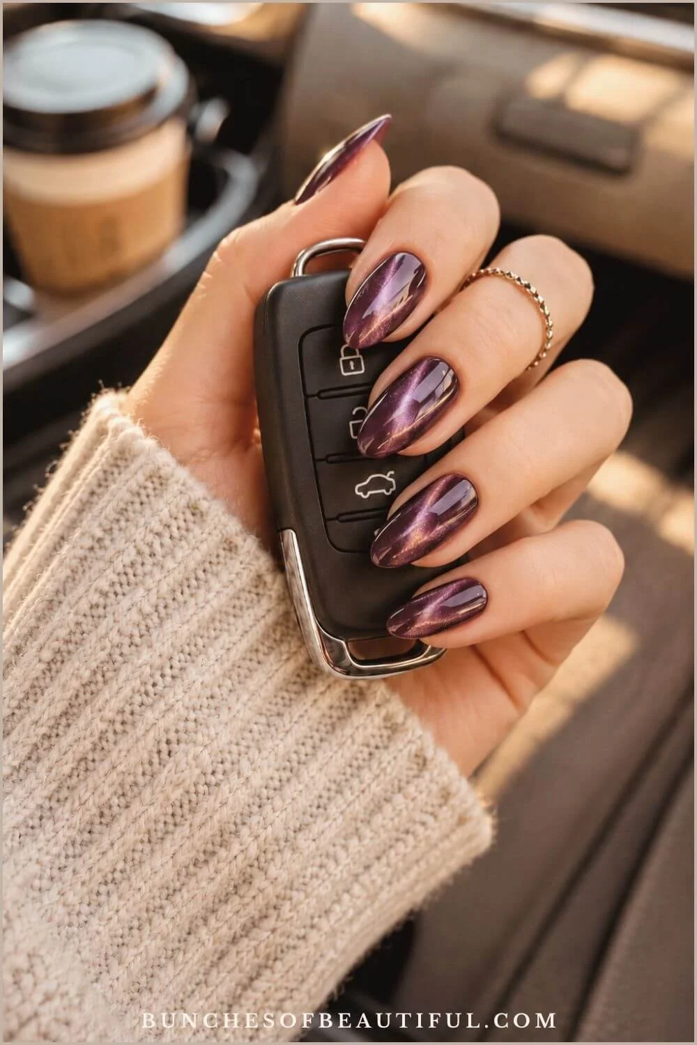 Glossy purple magnetic cat-eye nails with luminous diagonal highlights while holding a car key inside a vehicle.