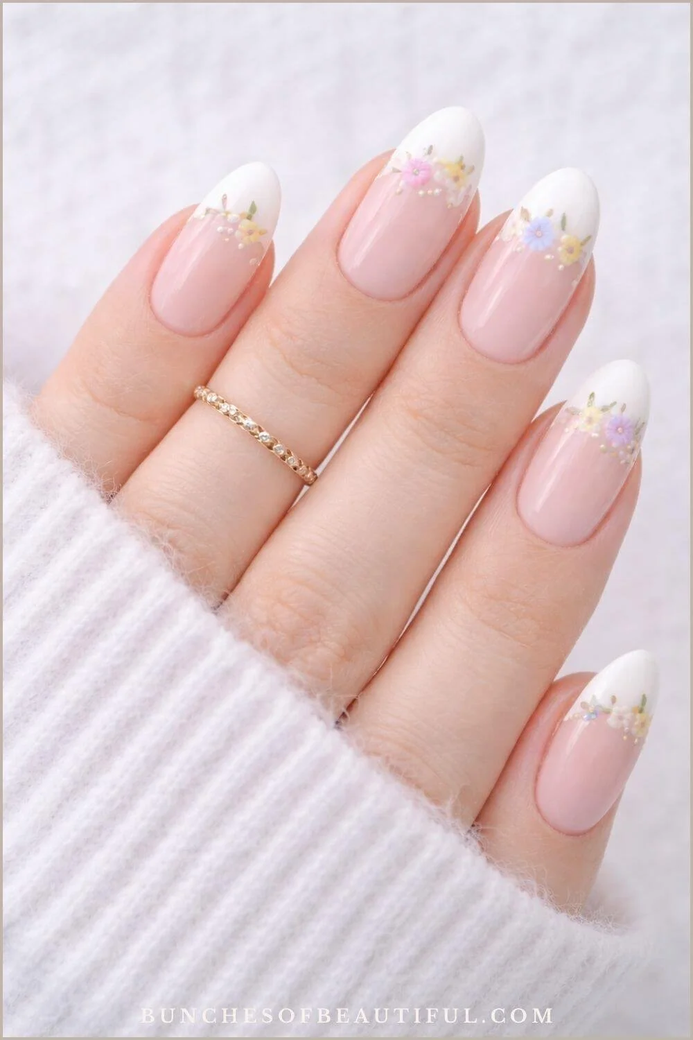 Almond shaped spring nails with soft pink base, white French tips, and tiny pastel floral accents with gold details.