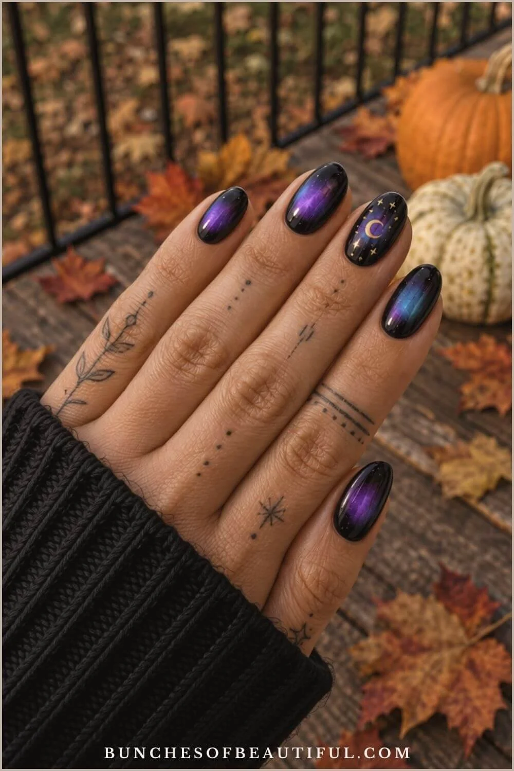 Black oval nails with glowing purple and blue aura effects, plus a gold crescent moon and stars, posed near fall pumpkins.