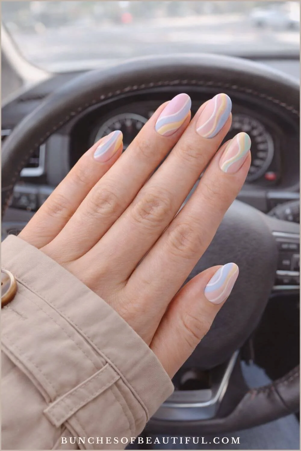 Pastel swirl spring nails with soft blue, yellow, peach, and lavender waves photographed inside a car.