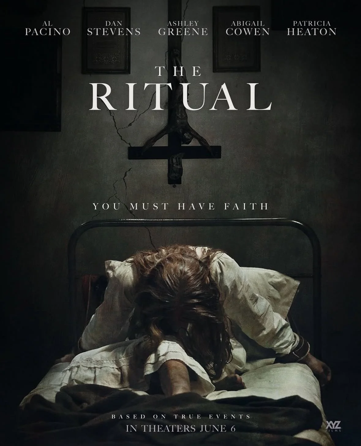 A woman with long hair leaning on a bed in a dimly lit room with cracked walls, with a large crucifix hanging above her. The poster includes the title "The Ritual" with actors' names and the release date, June 6.