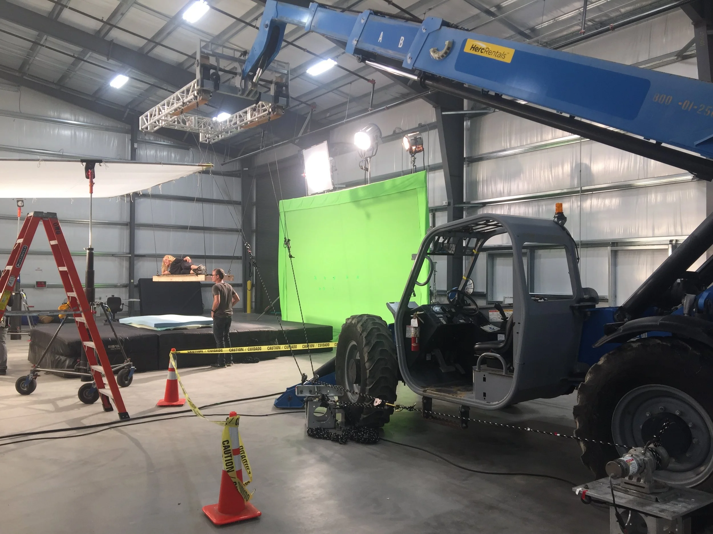 Filming studio with green screen, camera rig, lighting, and crew preparing for shoot in a warehouse