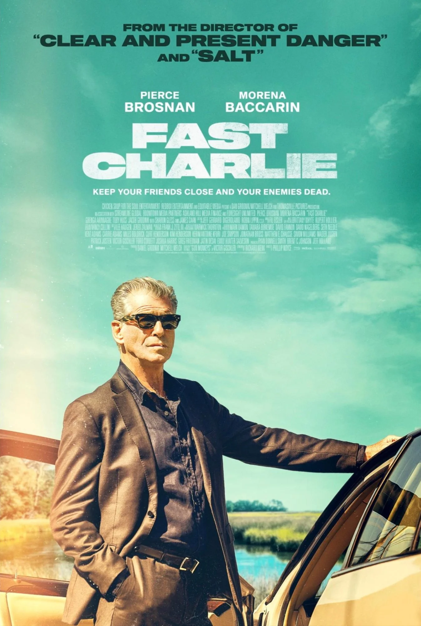 A movie poster for 'Fast Charlie' featuring a man in sunglasses and a black suit standing next to a car, with a scenic outdoor background and the movie title displayed at the top.