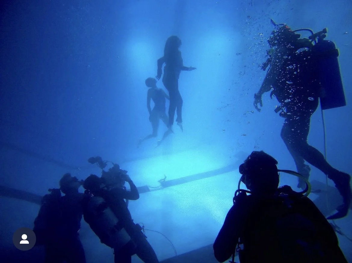 Divers and two women swimming underwater in a pool.