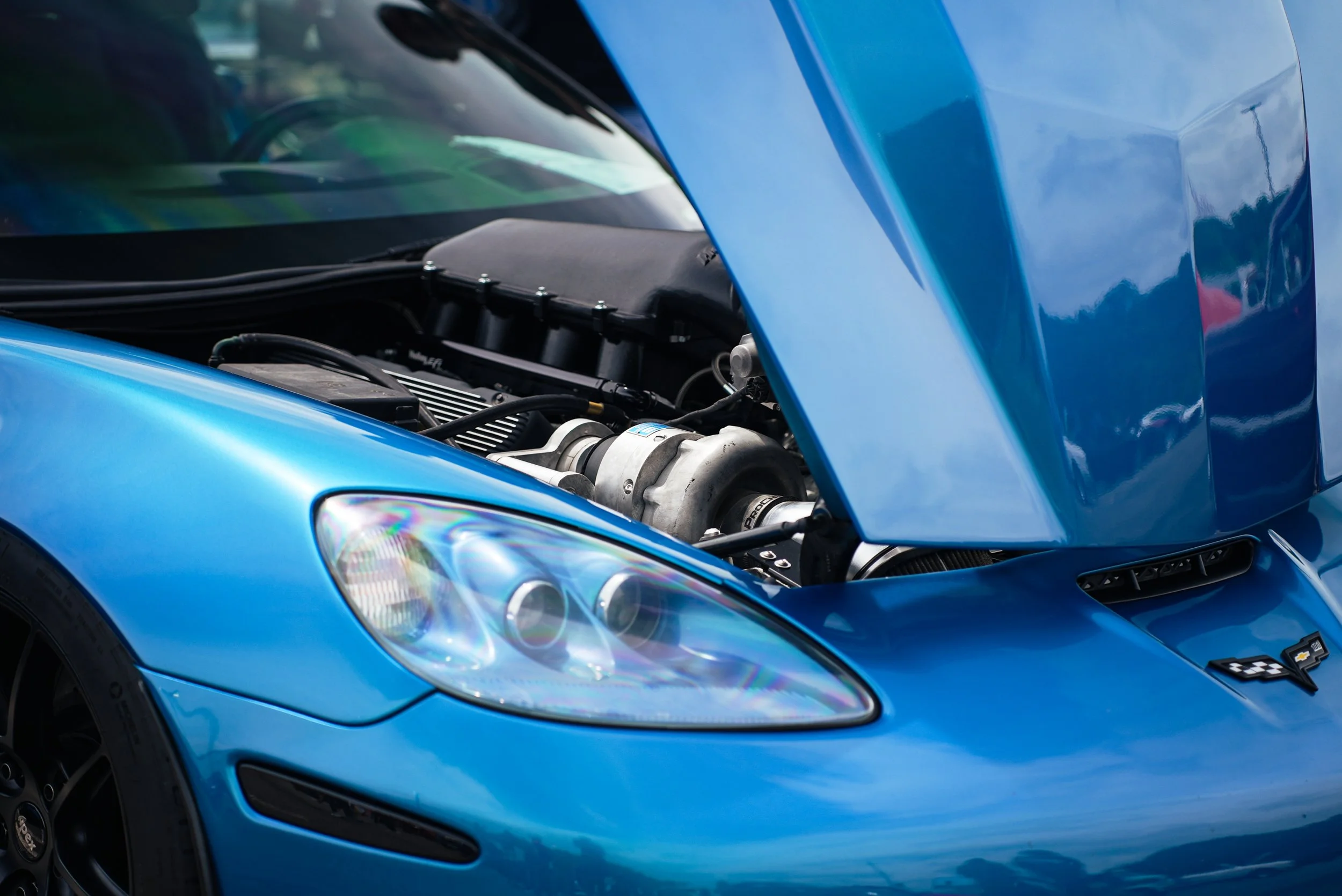 Close-up of a blue sports car with its hood open, revealing the engine compartment and headlight.