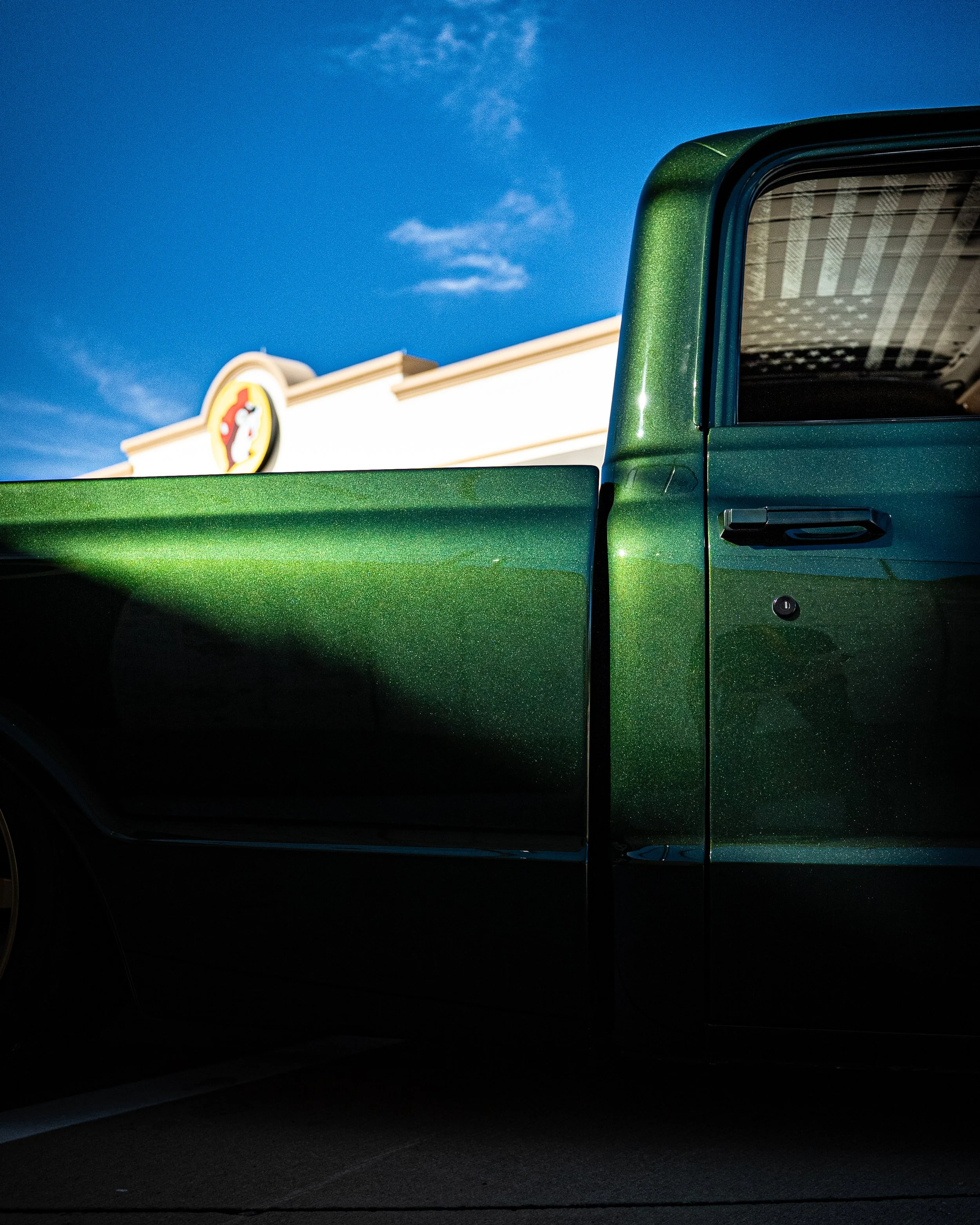 Close-up of the side of a metallic green pickup truck against a blue sky with a building in the background displaying the Yellow Pages sign.
