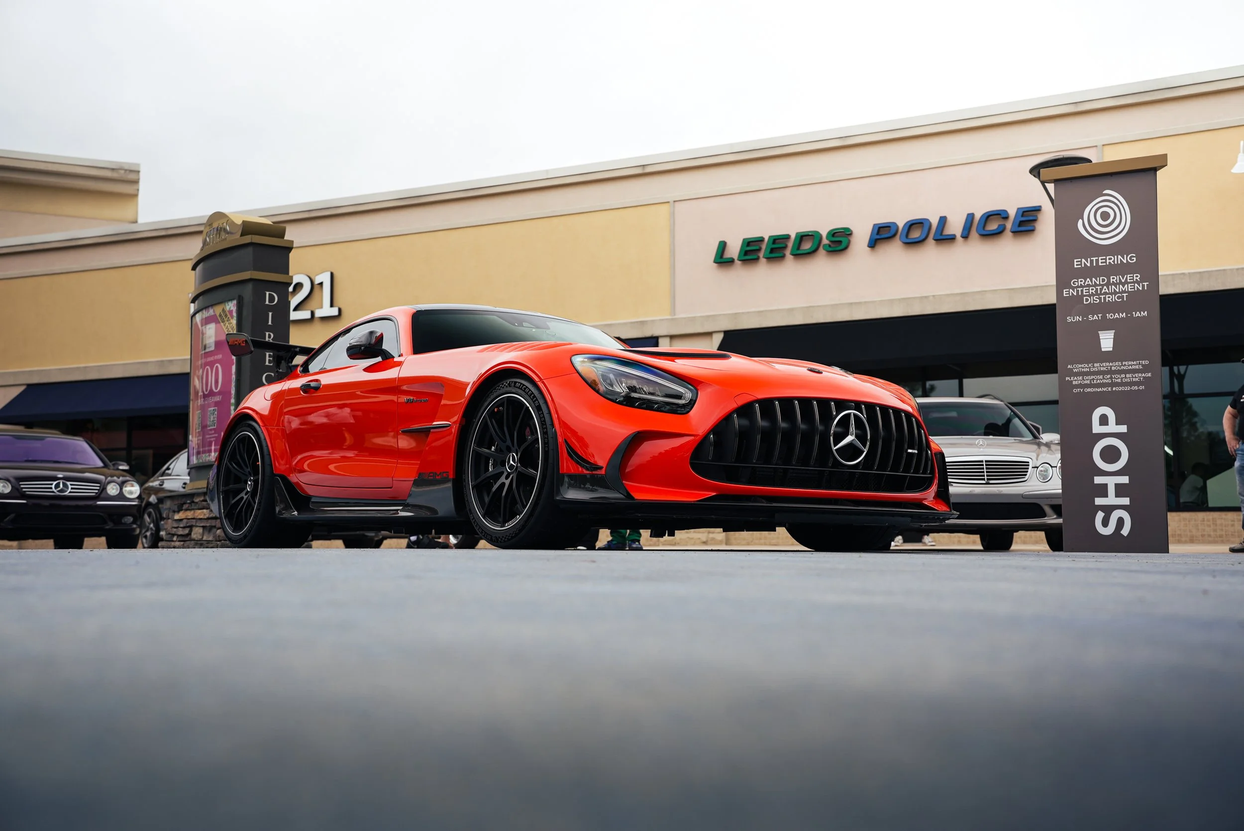 A bright red Mercedes-Benz sports car parked in front of Leed's Police building with a sign for the Grand River Entertainment District.