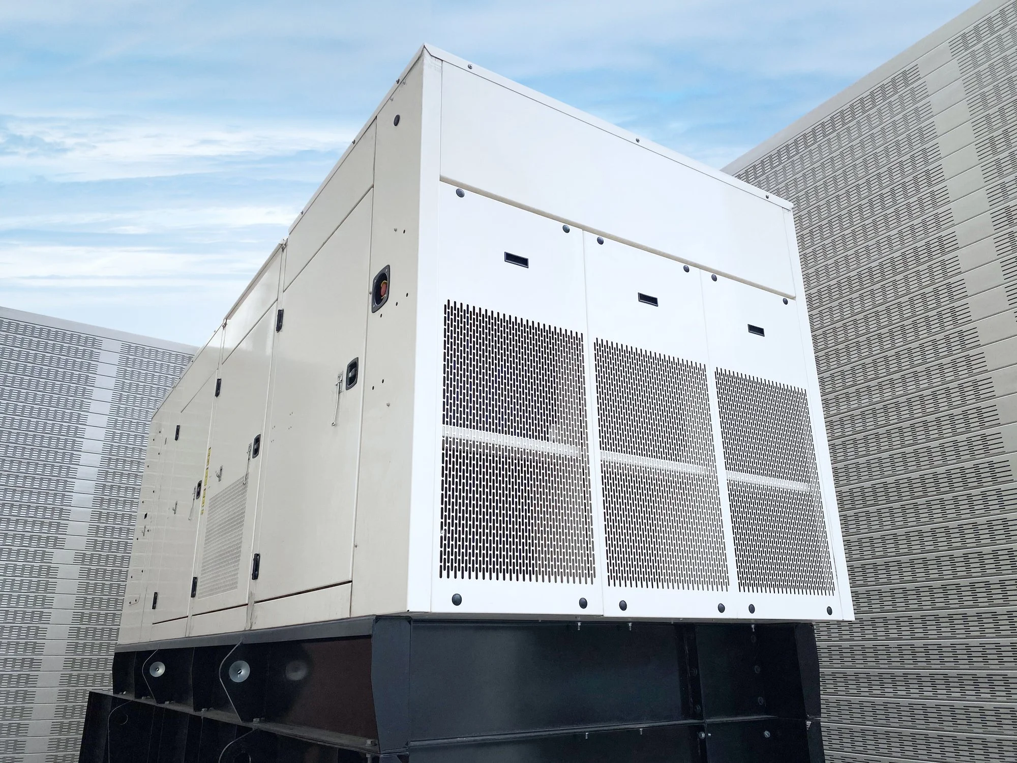 Large white industrial generator on a rooftop with a cloudy sky in the background.