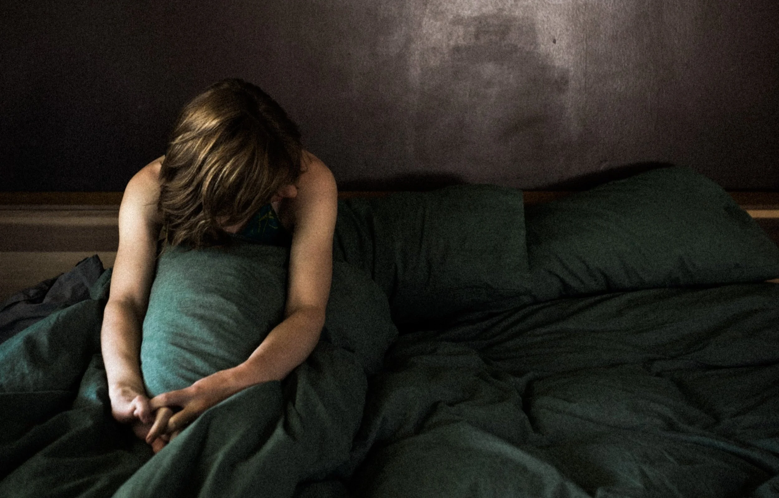 Woman (Jacquelyn) sitting up in bed, looking to the side, pensively.
