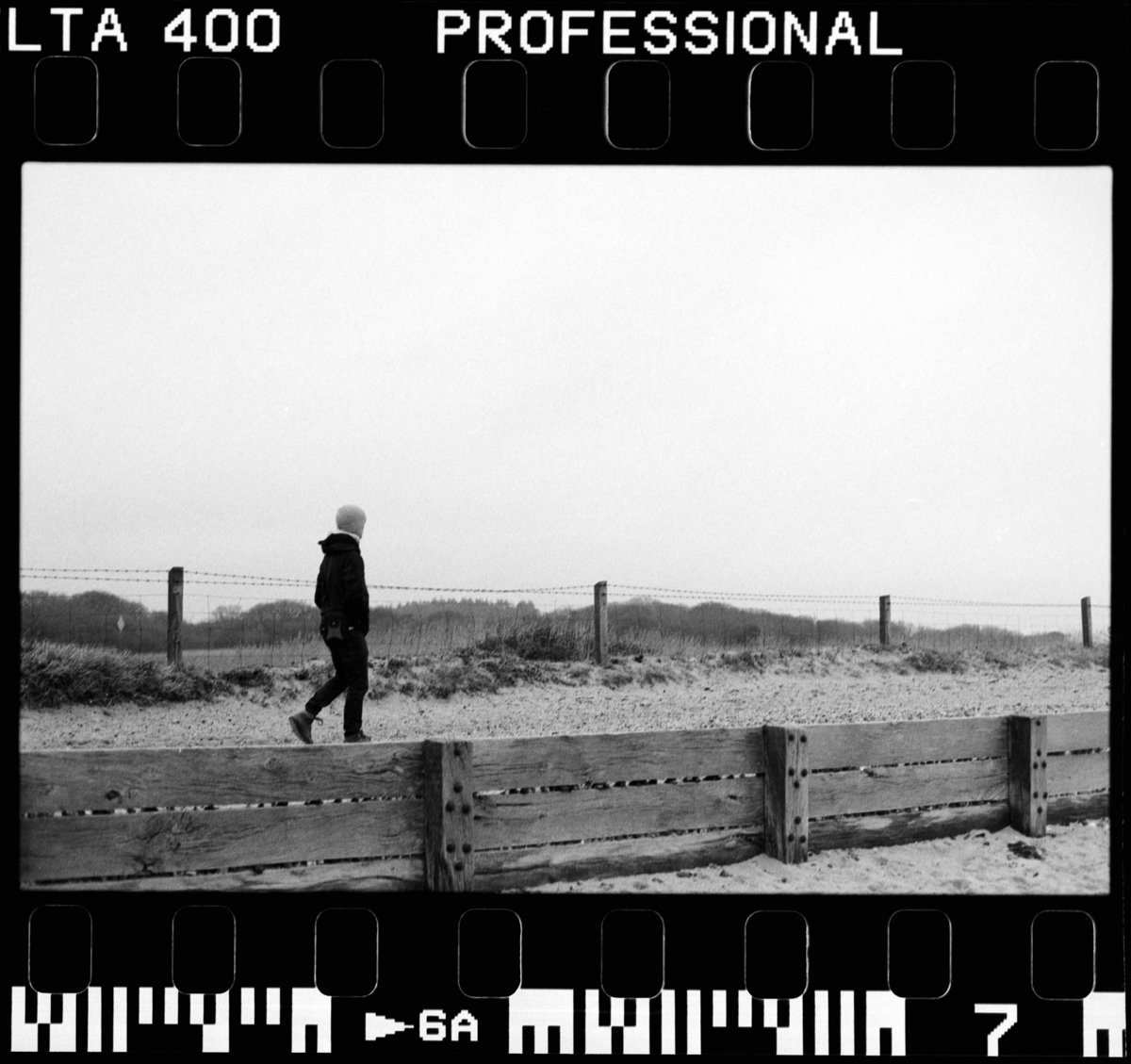 Grainy black and white film photo of a man walking by the coast
