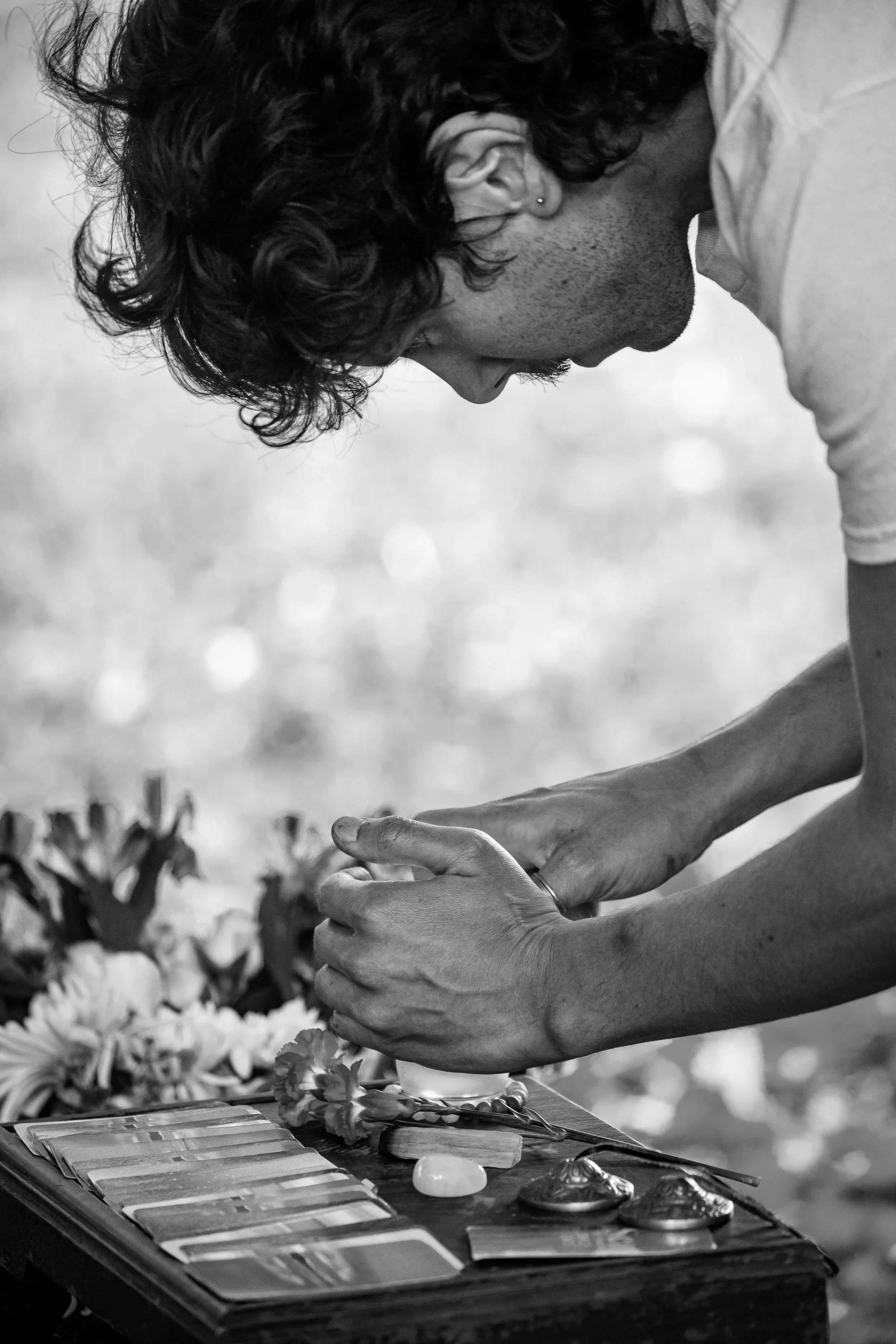 A man placing his hands together in a prayer position over a table with flowers, jewelry, and cards, during a memorial or tribute ceremony.