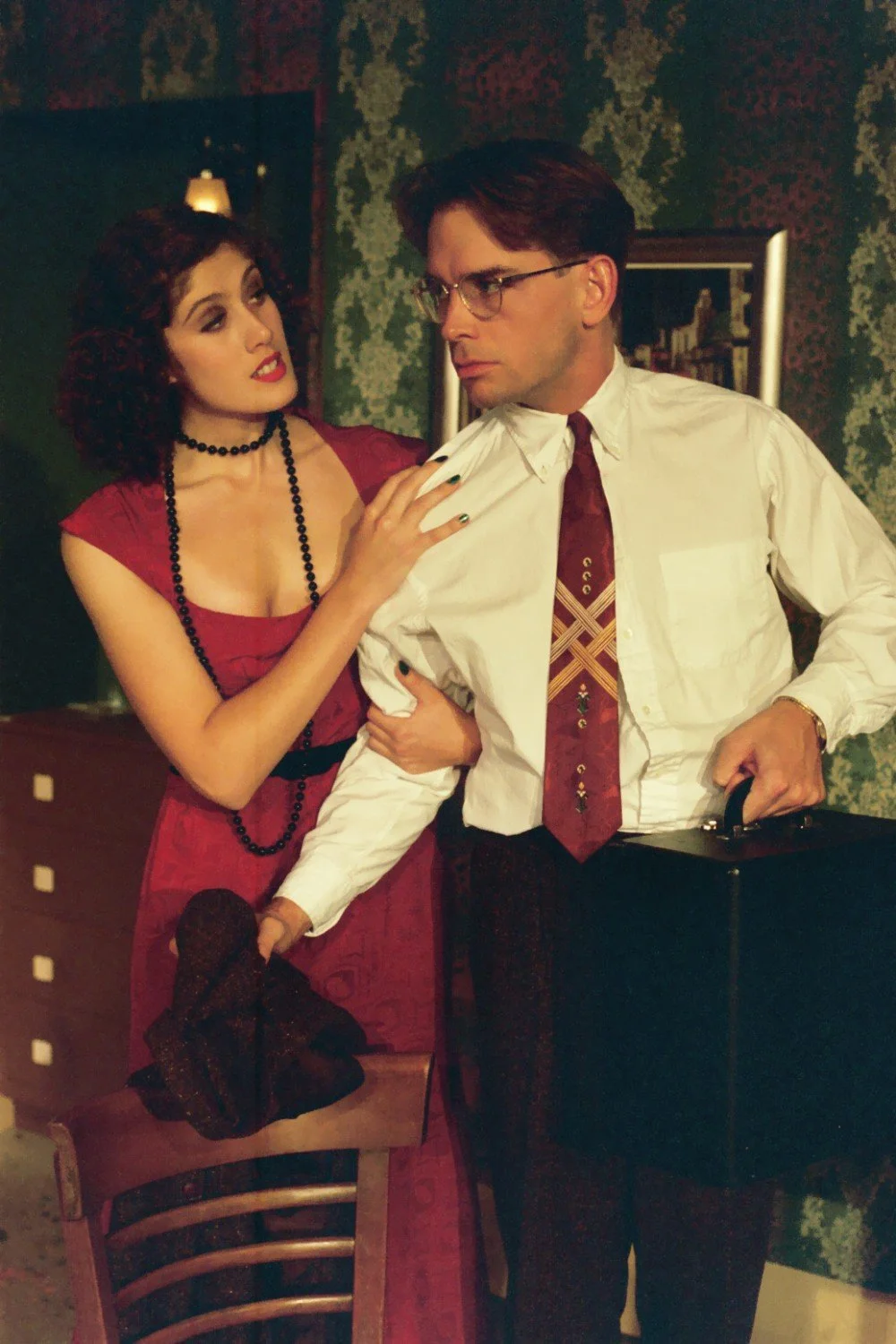 A woman in a red dress holding a man in glasses and a white shirt, who is holding a briefcase.