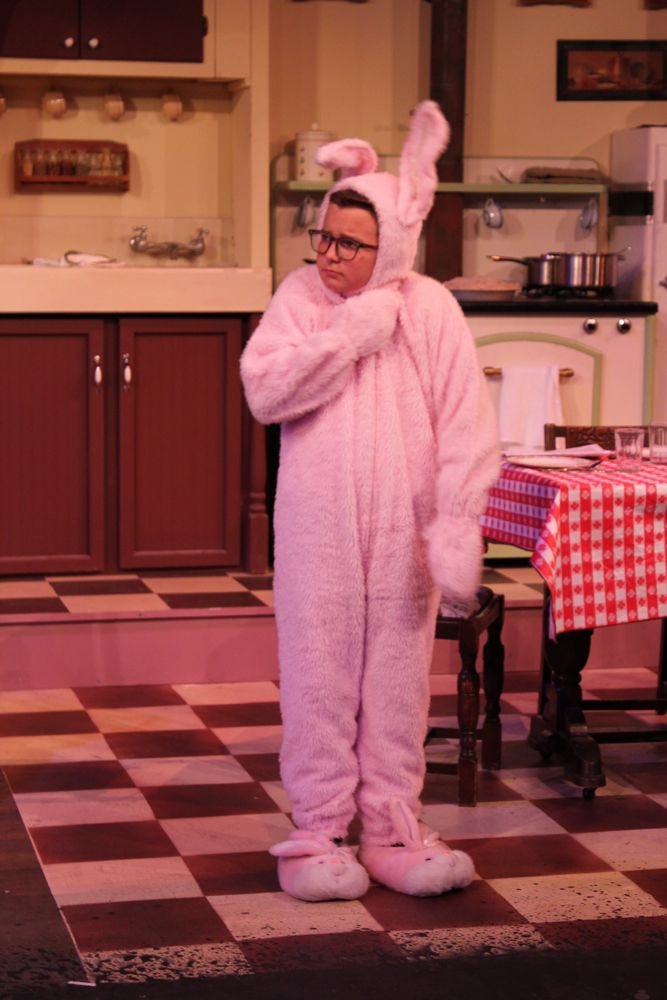 Person in pink bunny costume standing in a kitchen with checkered floor, wearing glasses.