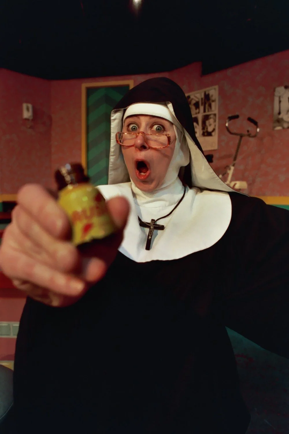 A woman dressed as a nun holding a small bottle with a surprised expression.