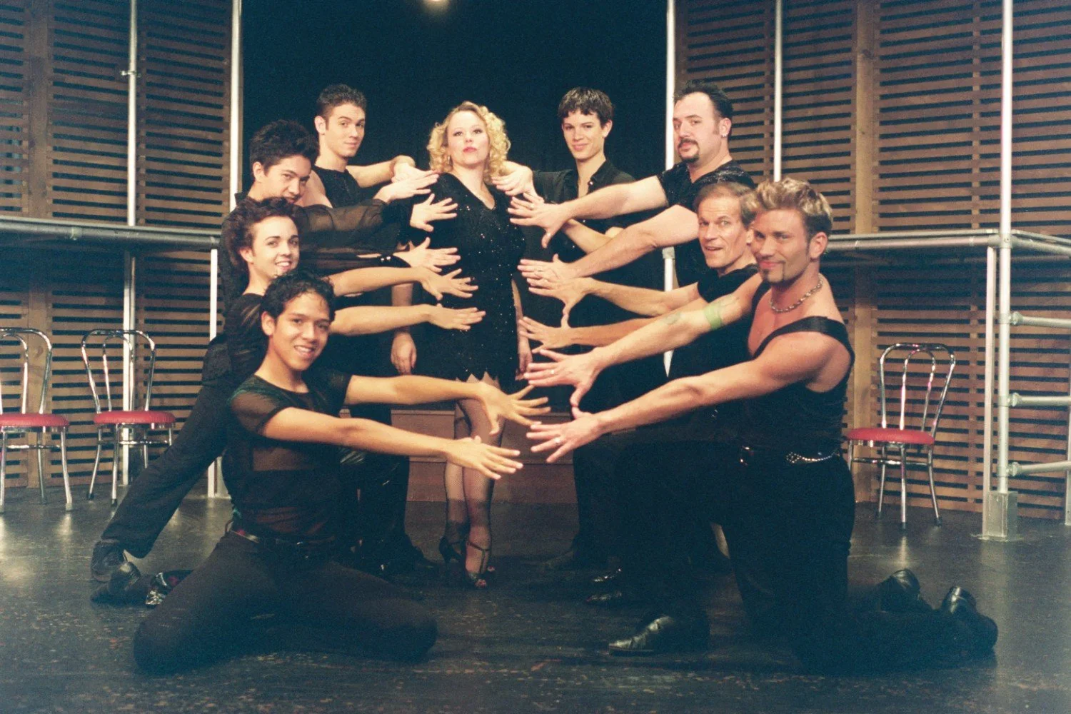 Group of performers in a theatrical pose with a woman in the center.