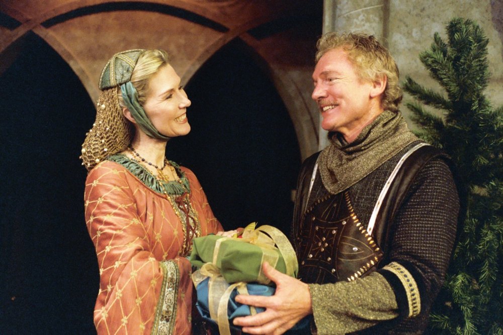 Two people in medieval costumes exchanging a gift in a festive setting.