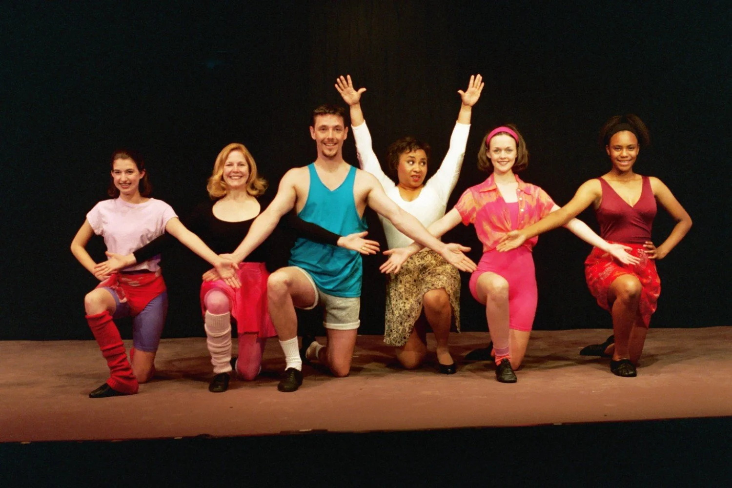 Group of six performers in colorful dance attire striking a pose on stage.