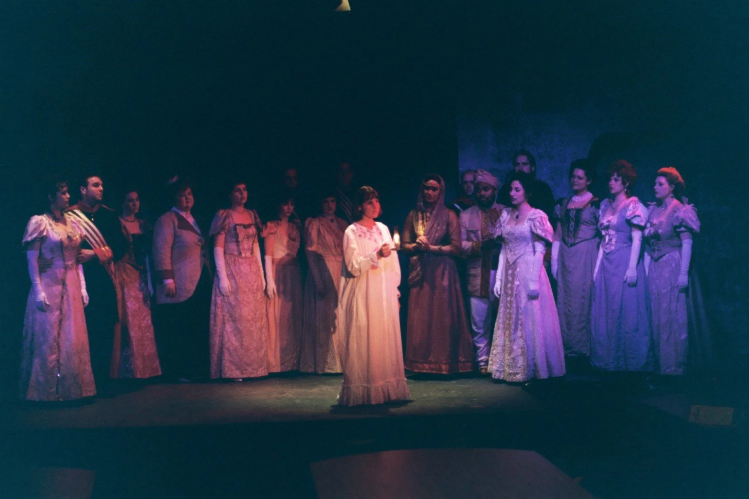Theater performance with a group of actors in period costumes, one holding a candle