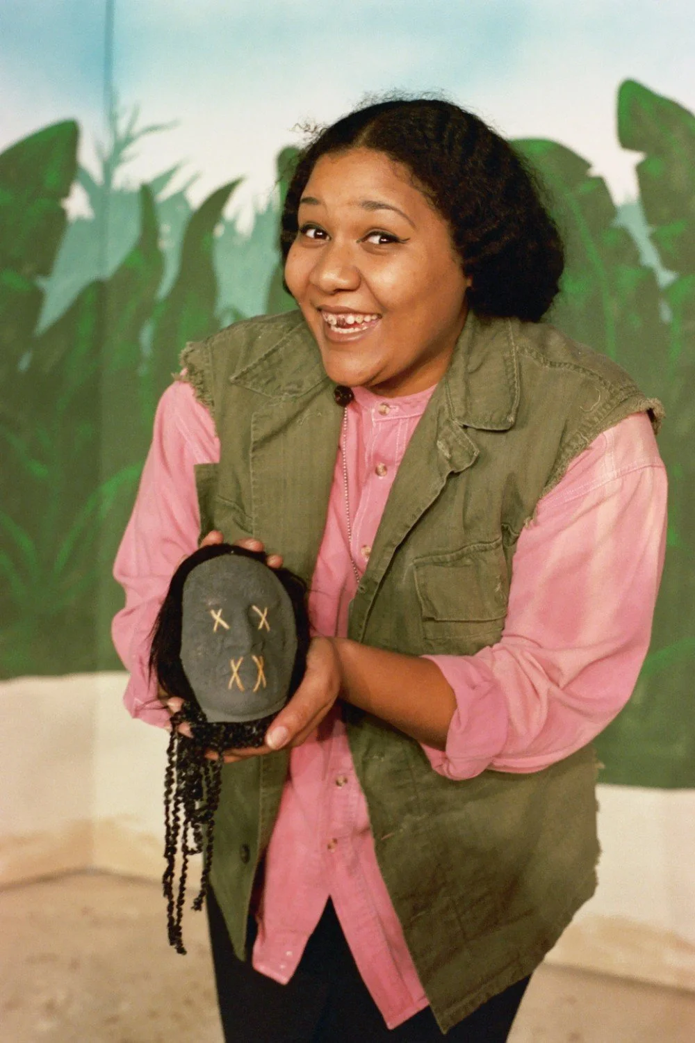 Smiling person holding a small, handmade puppet with stitched features and black yarn hair.
