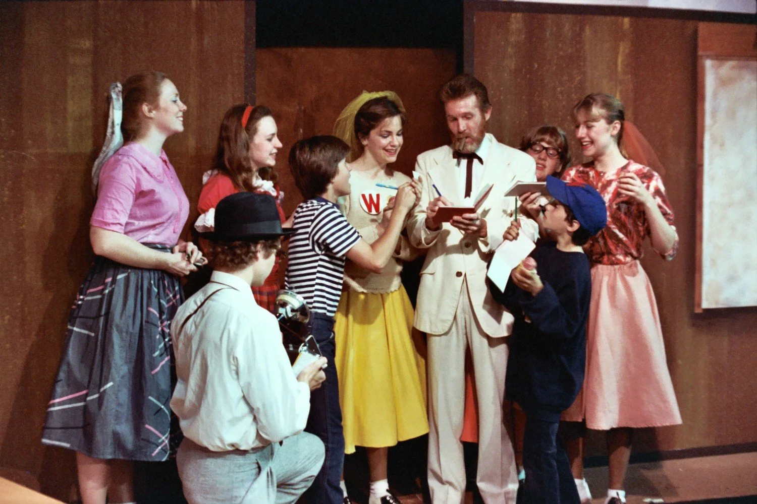 Group of people in vintage costumes gathering around a man in a white suit, indoors.