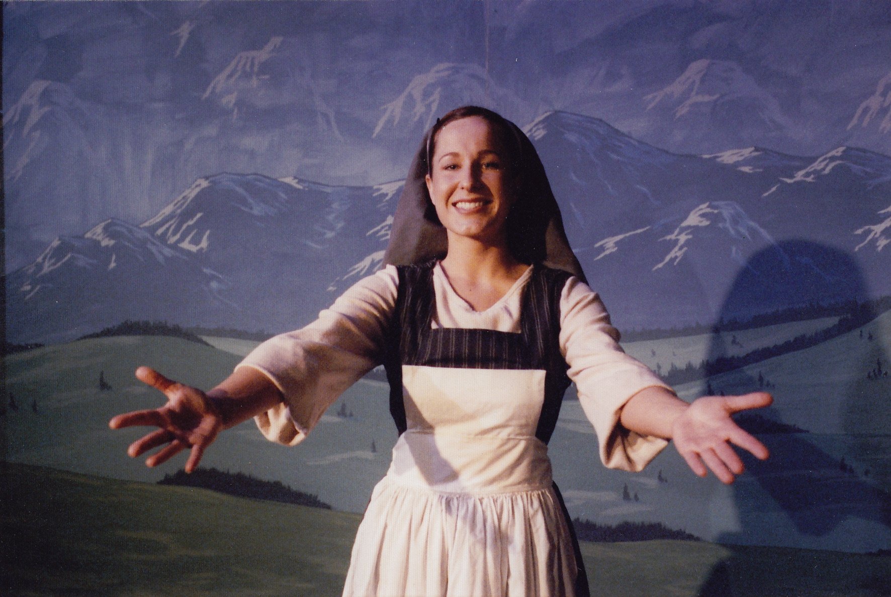 Person in a nun costume performing on stage with a mountain backdrop.