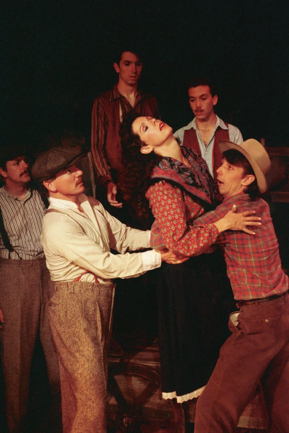 Stage performance with actors in period costumes, including a woman being supported by two men, with three other men looking on.