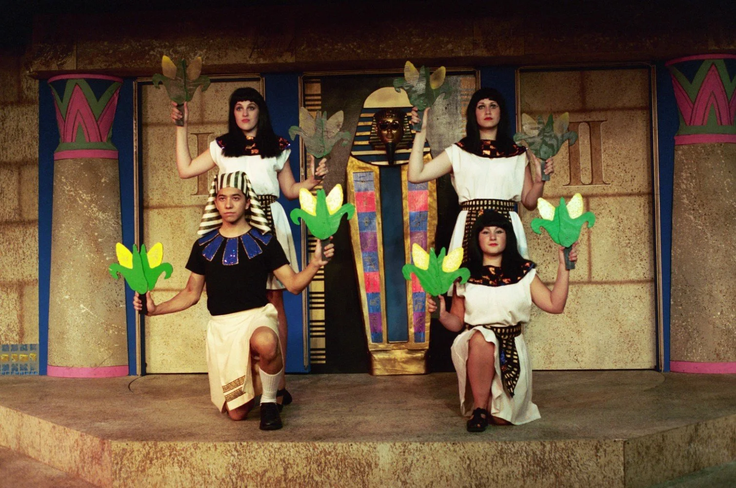 Group of people in ancient Egyptian costumes performing on stage with papyrus props