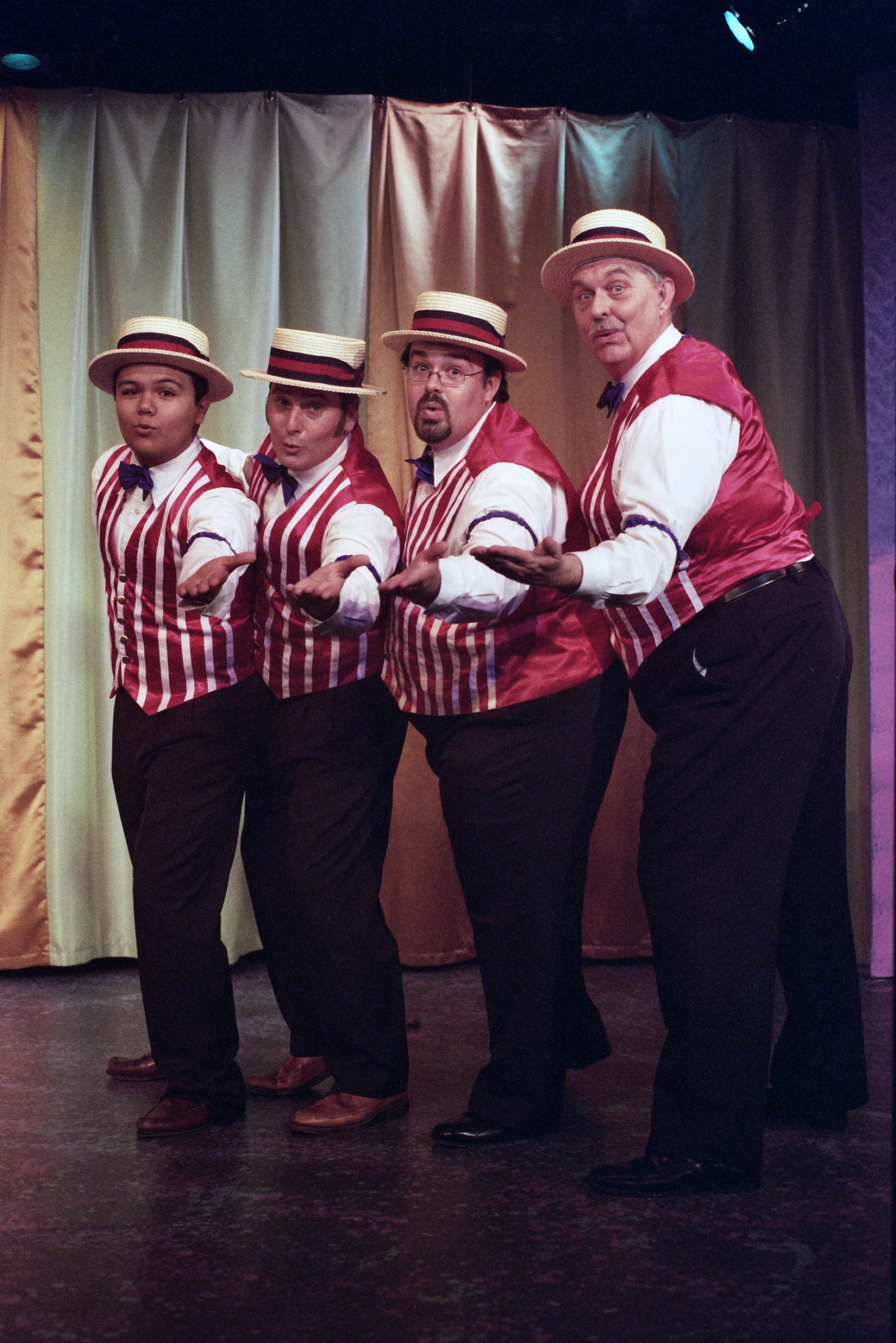 Four men wearing red and white striped vests and straw boater hats performing on stage.