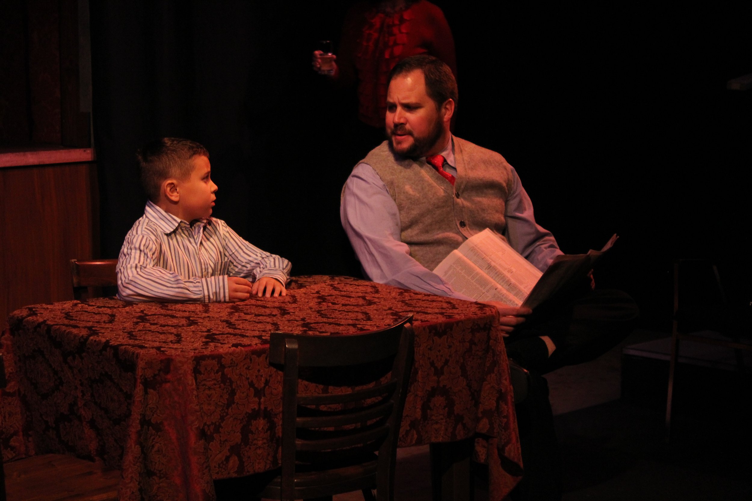 Child and man sitting at a table with a book in a dark room