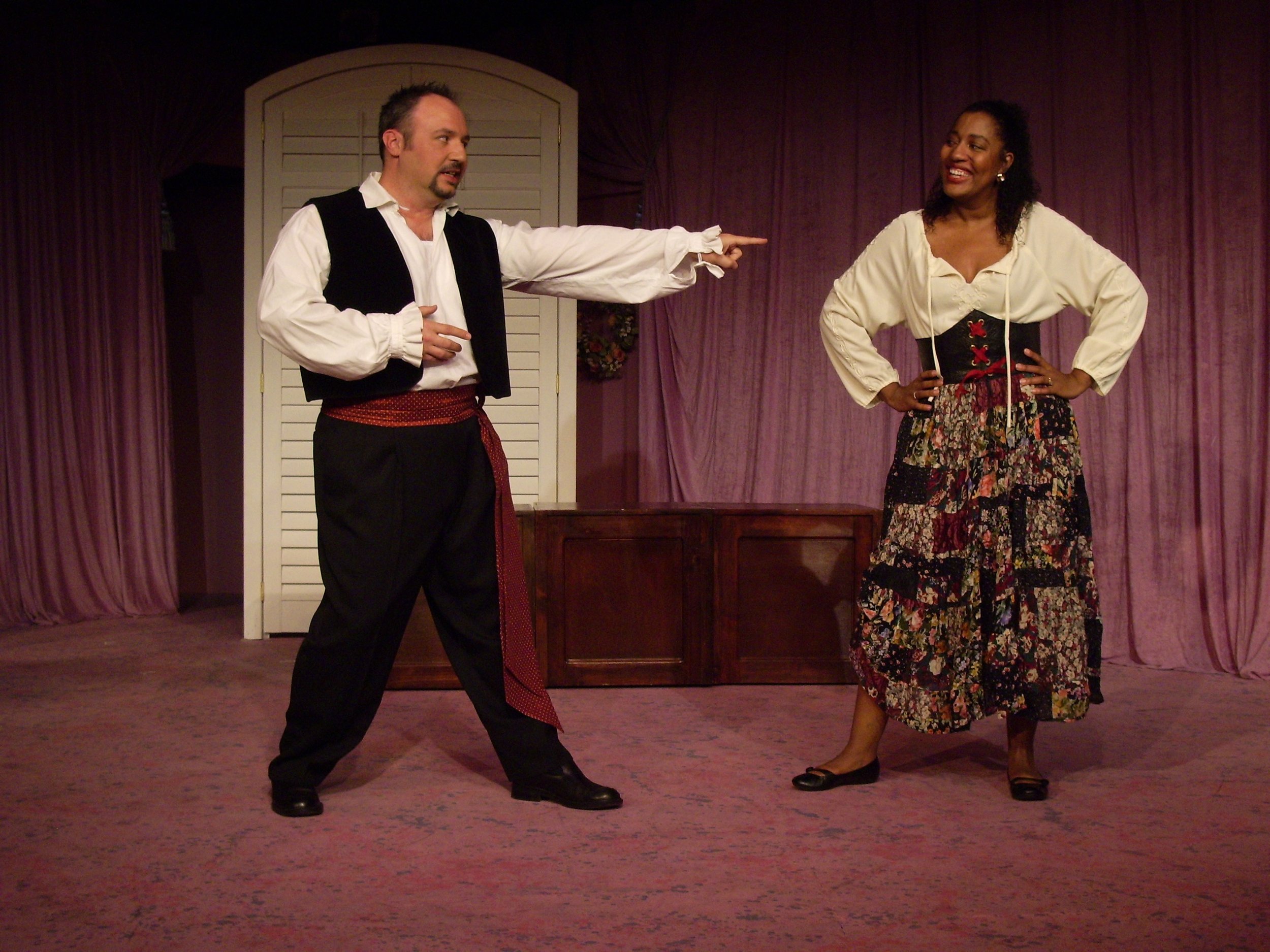 Two actors in period costumes performing on stage with a purple curtain backdrop.