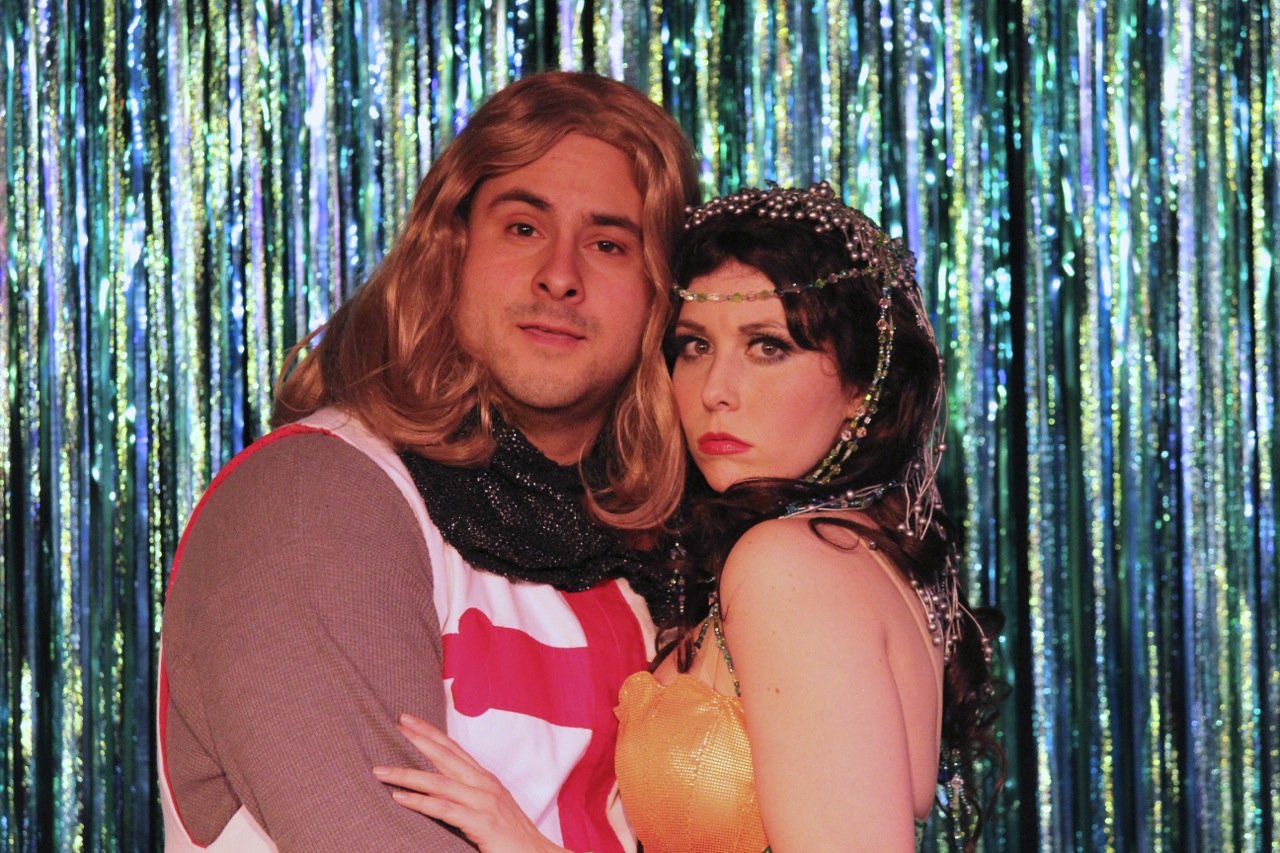 Two people in costumes posing in front of a shiny backdrop