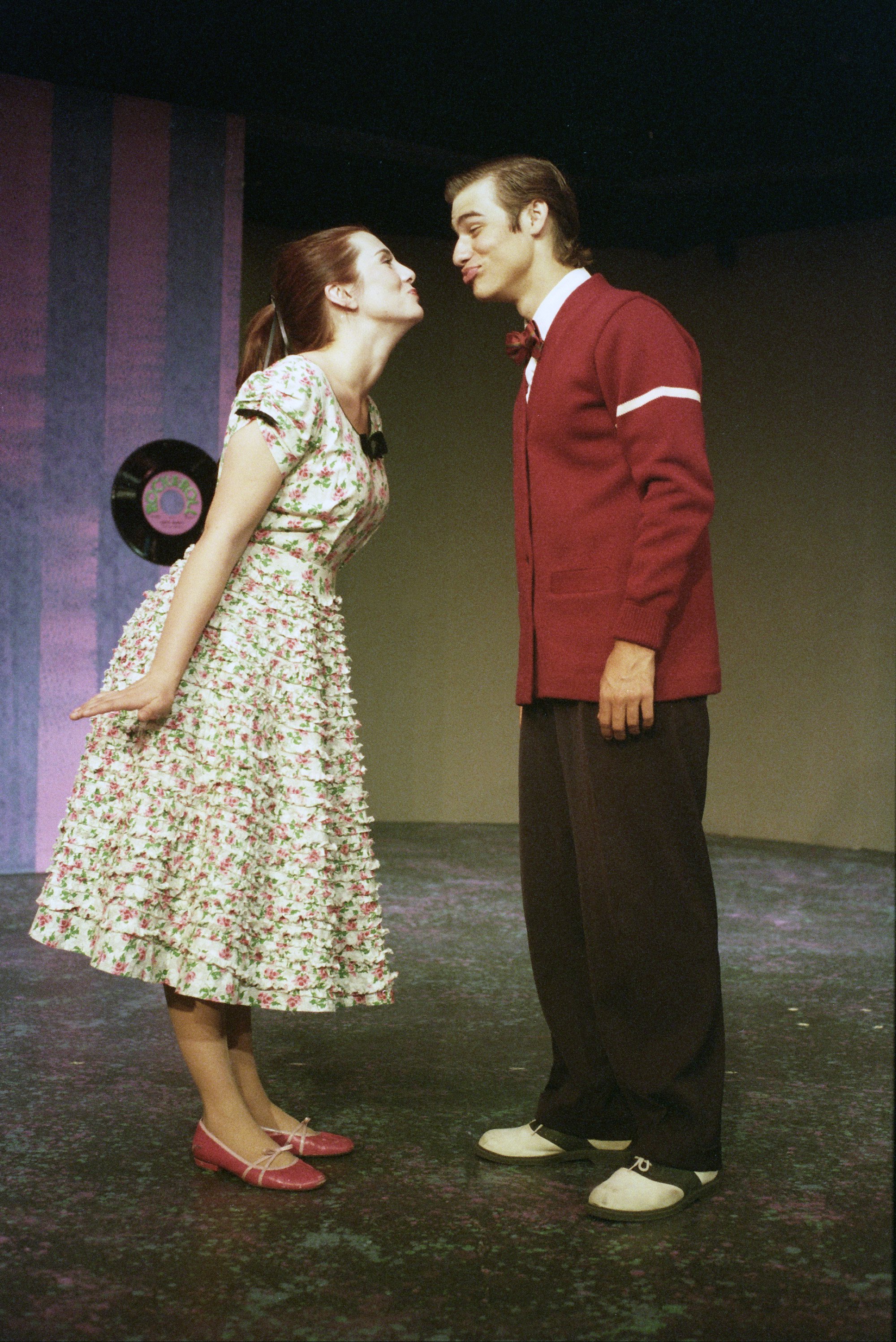 A man and a woman in vintage attire making playful faces on a stage.