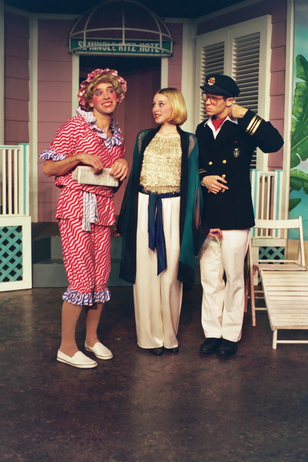Three actors in a comedic play set at the Seminole Ritz Hotel. One is dressed in a red and white striped dress with a bonnet, another in a shimmering top and white pants, and the third in a naval officer's uniform.