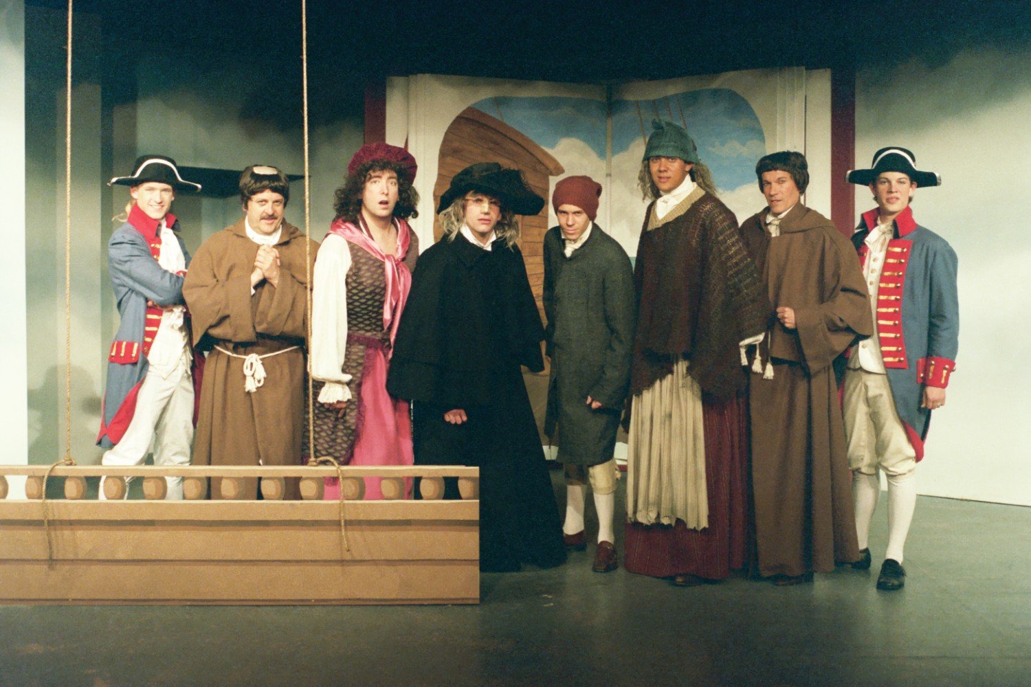Actors in historical costumes on a stage with an open book backdrop, depicting a theatrical performance.