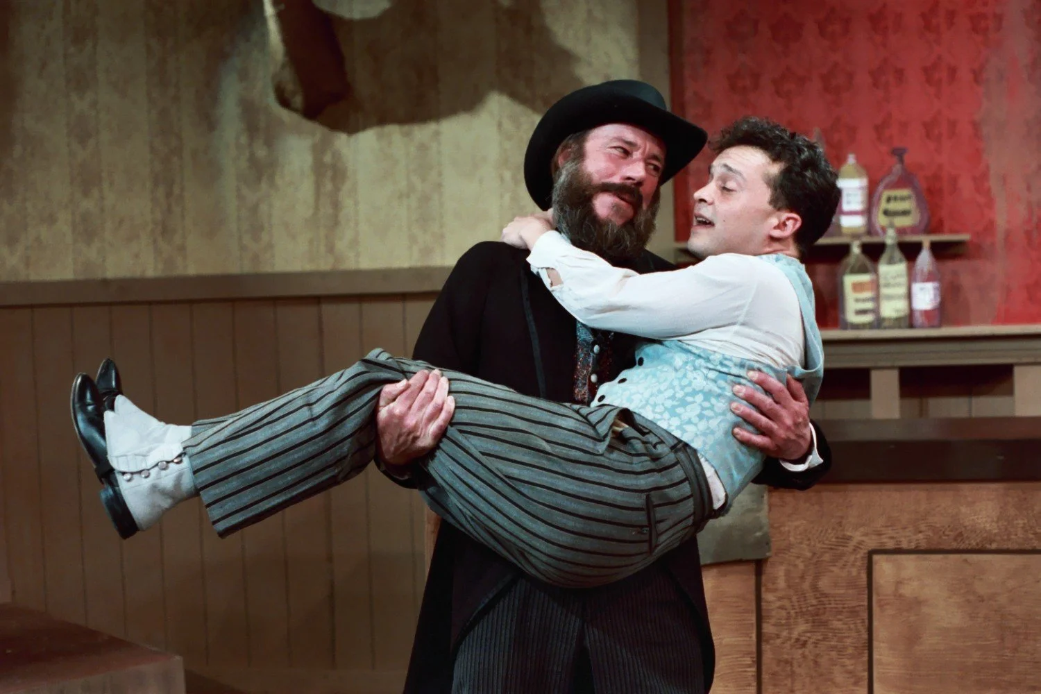 A man in a period costume holding another man in a theatrical setting.