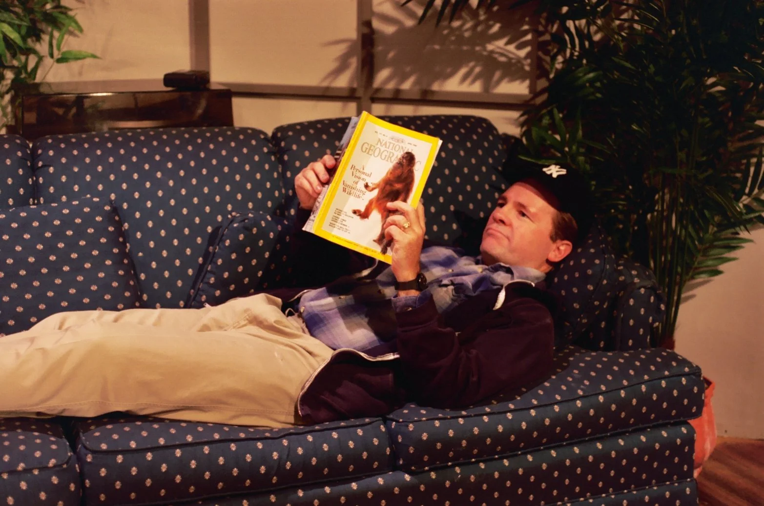 Man on couch reading National Geographic magazine