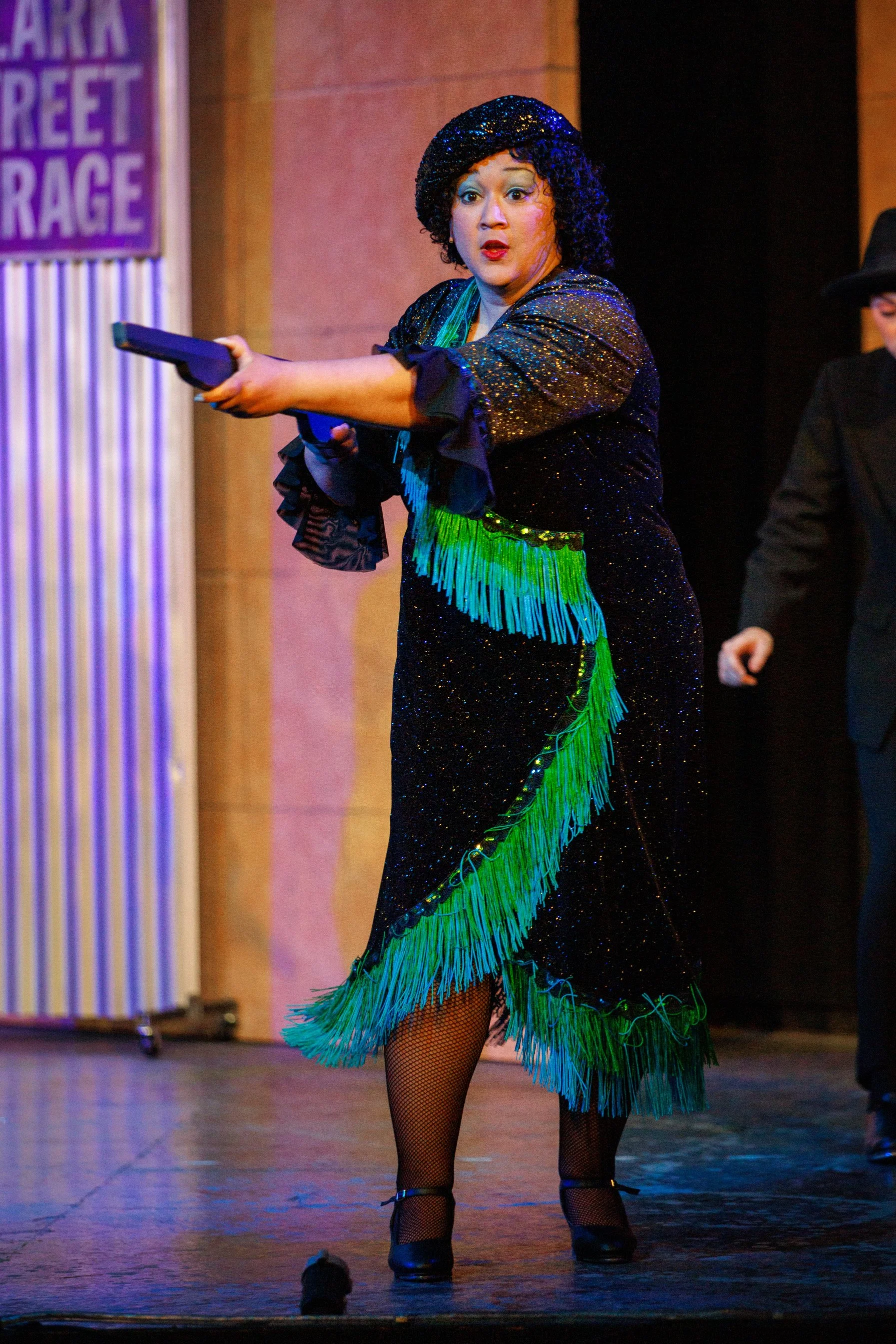 Performer in flapper costume holding a prop gun on stage