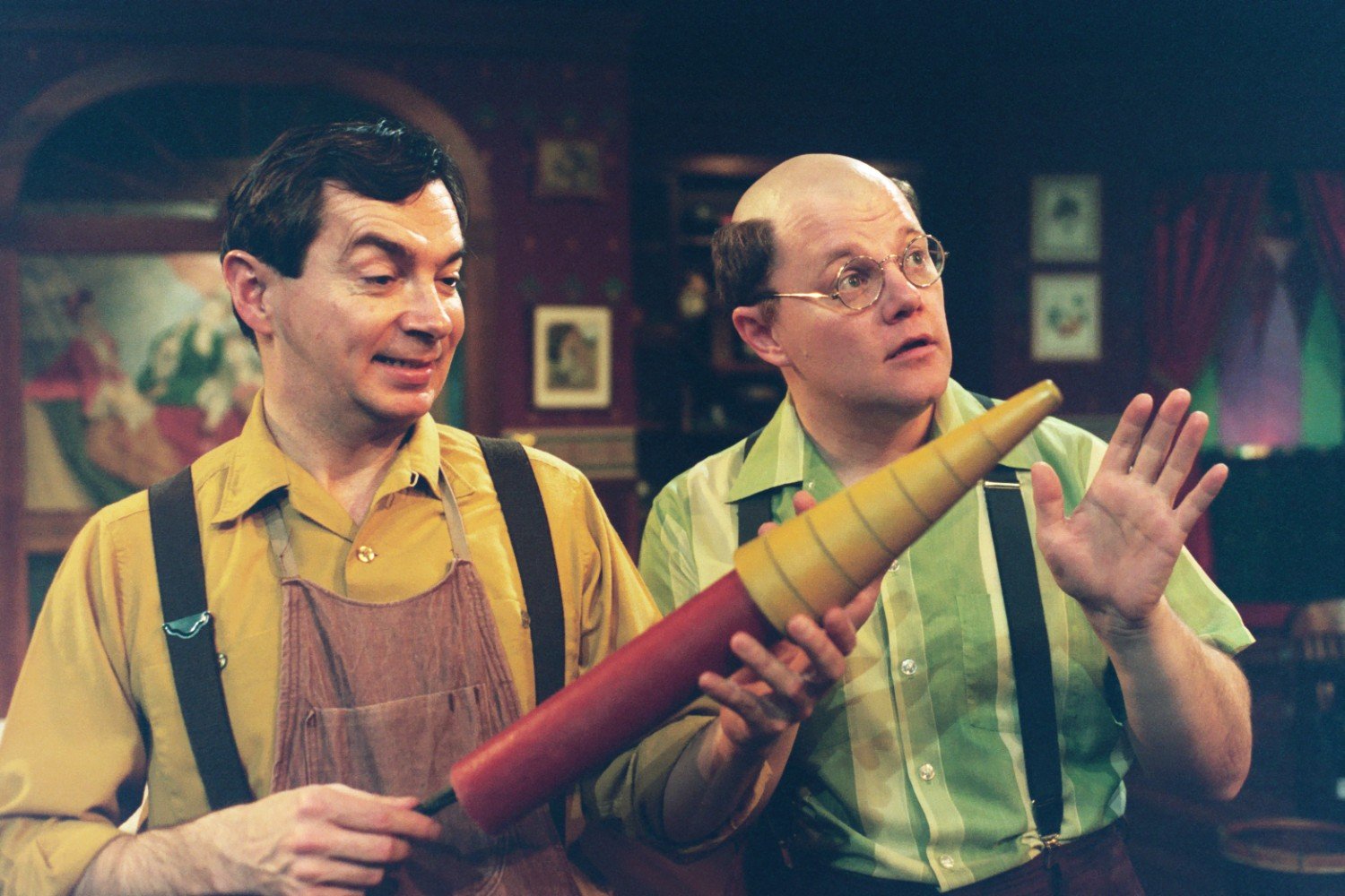 Two men in vintage clothing holding a large orange and yellow cone object.